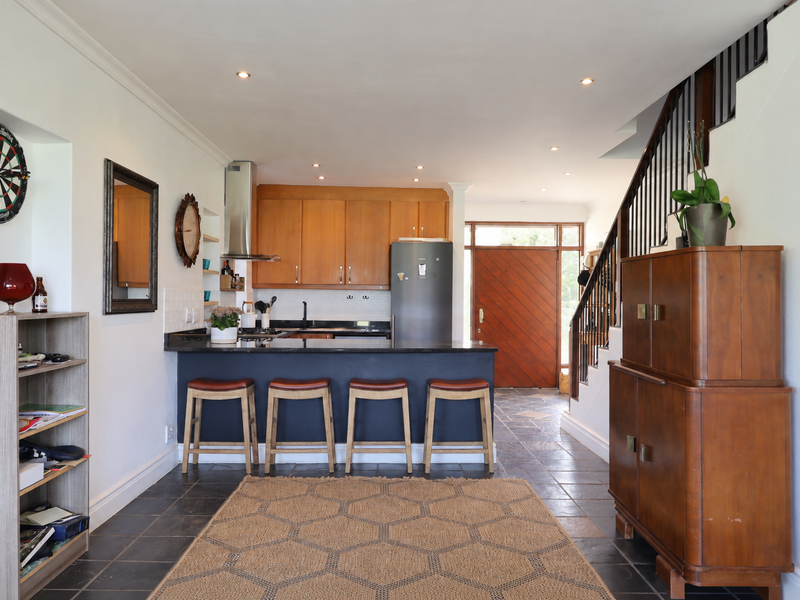 Open-plan kitchen and living area featuring dark stone countertops, wooden cabinetry, tiled flooring, and a staircase leading to the upper level.
