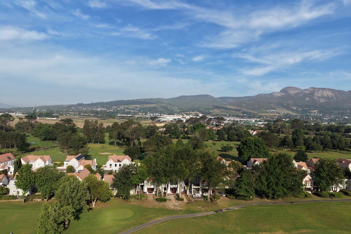 An elevated aerial view of a residential estate situated alongside a golf course, featuring scenic mountain views in the background.