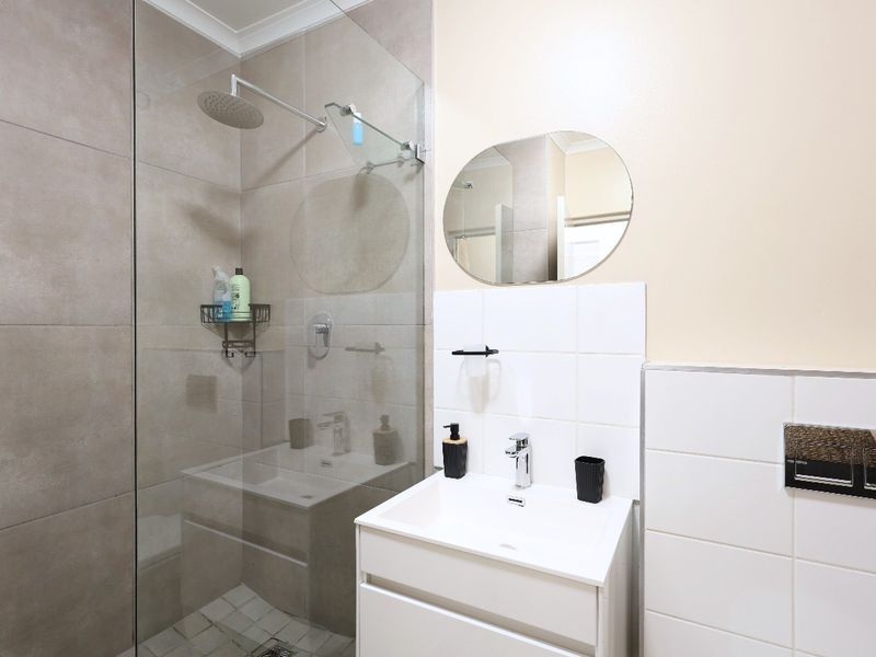 Modern bathroom featuring a walk-in shower with a glass screen, rain shower head, and a sleek vanity unit with a basin.