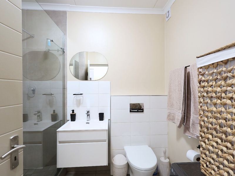 Modern bathroom featuring a wall-mounted vanity, wall-hung toilet with concealed cistern, and a glass-enclosed shower with neutral tiling.