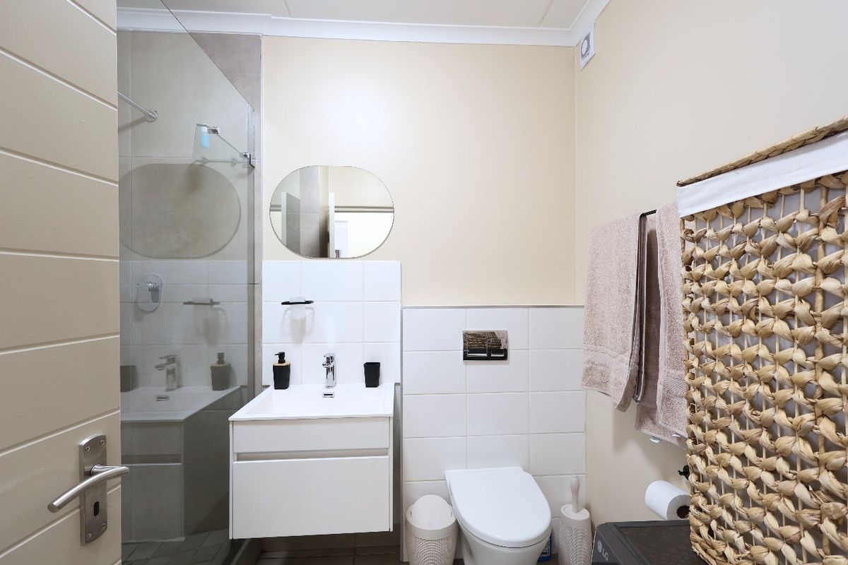 Modern bathroom featuring a wall-mounted vanity, wall-hung toilet with concealed cistern, and a glass-enclosed shower with neutral tiling.