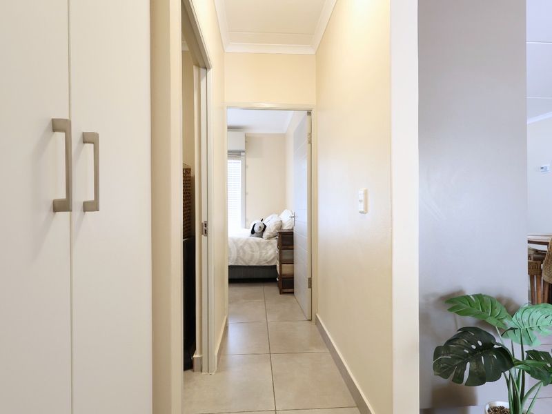 A clean, well-lit hallway featuring neutral tiled flooring and built-in storage cupboards, providing access to adjacent rooms within the apartment.
