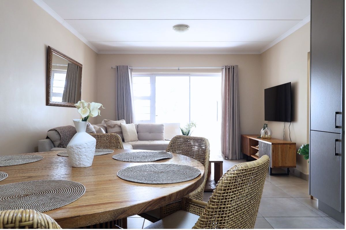 A bright open-plan living and dining area featuring tiled flooring, neutral walls, and a large sliding glass door providing natural light.