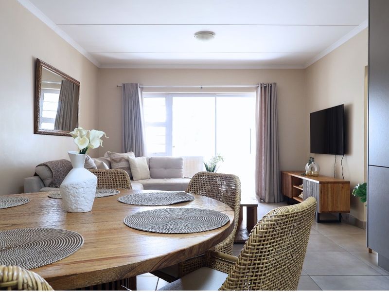 A bright open-plan living and dining area featuring tiled flooring, neutral walls, and a large sliding glass door providing natural light.