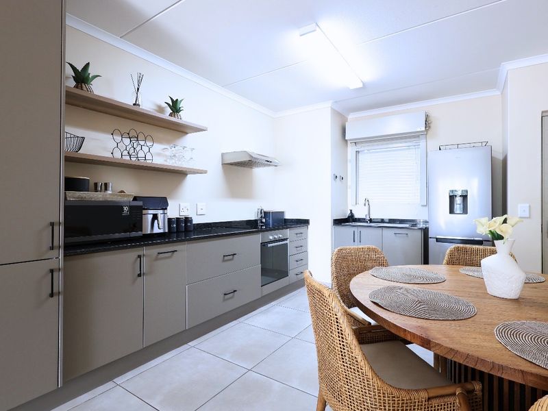 Modern open-plan kitchen featuring sleek cabinetry, granite countertops, integrated oven, and extractor fan, seamlessly flowing into the dining area with tiled flooring throughout.
