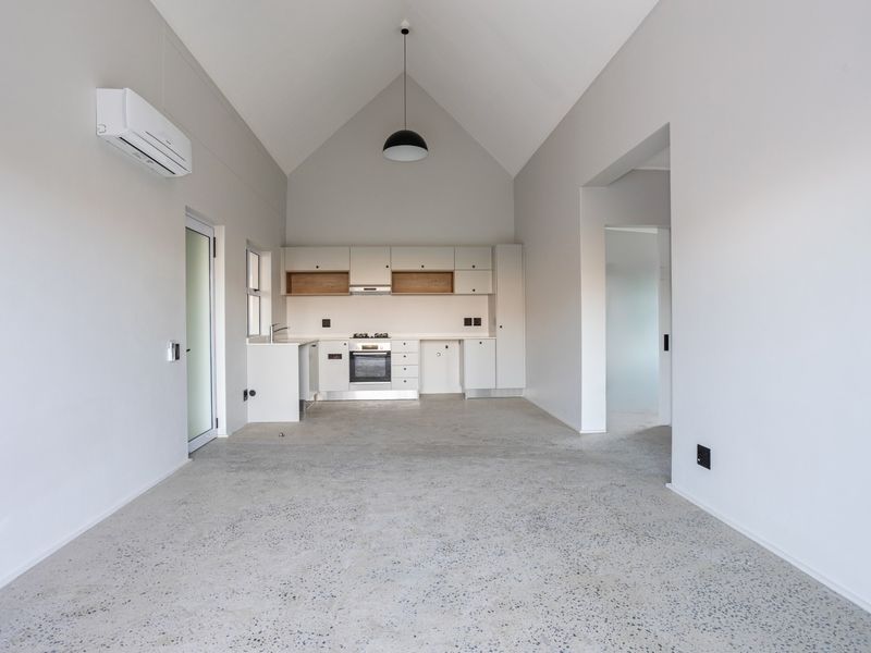Modern open-plan living area featuring a high vaulted ceiling, polished concrete floors, and a sleek, minimalist kitchen with integrated appliances.