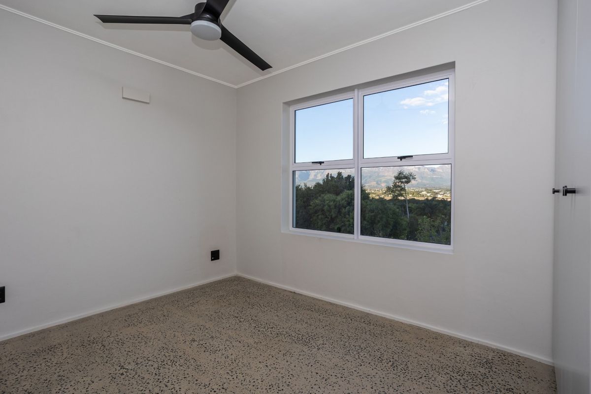A bright, empty bedroom featuring terrazzo flooring, a modern ceiling fan, and a window offering scenic mountain views.