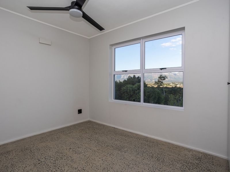 A bright, empty bedroom featuring terrazzo flooring, a modern ceiling fan, and a window offering scenic mountain views.