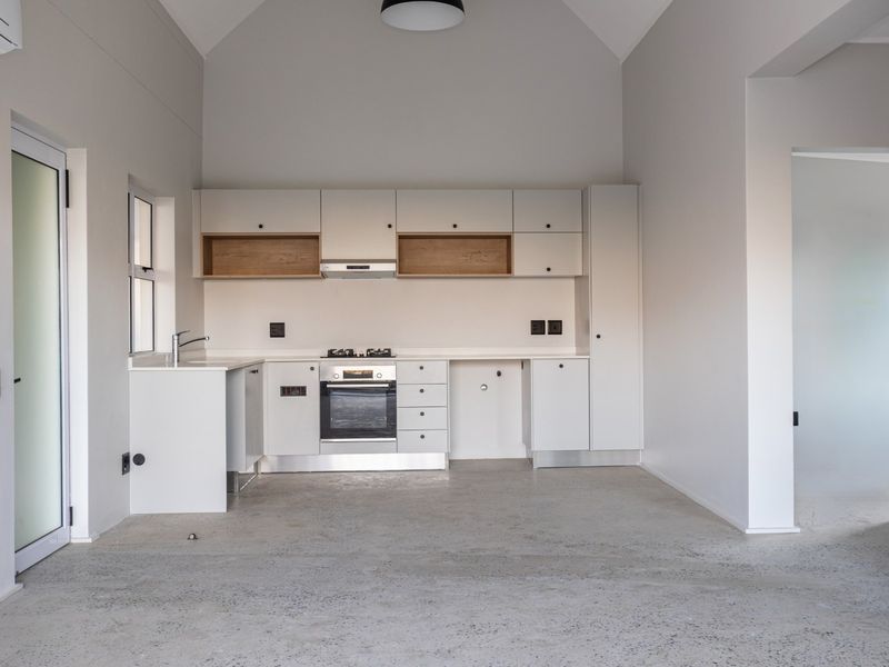 Modern open-plan kitchen featuring sleek white cabinetry, integrated oven and hob, polished concrete flooring, and a high vaulted ceiling in a minimalist space.