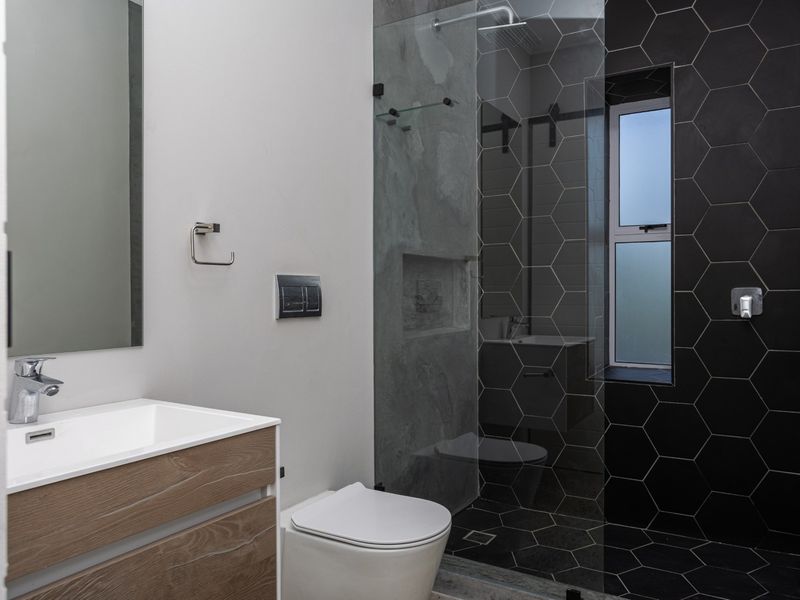 Modern bathroom featuring a wood-finish vanity, wall-mounted toilet, and a walk-in shower with striking black hexagonal tiling and a recessed niche.