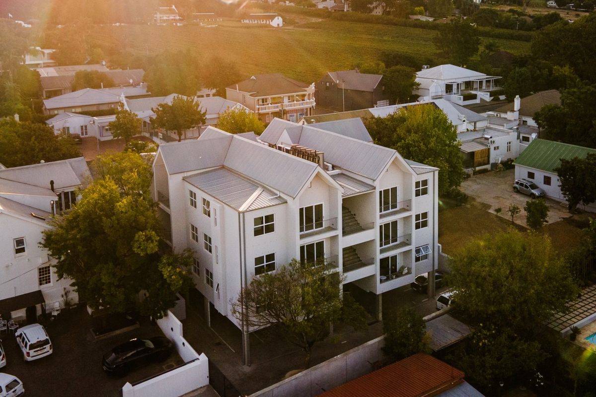 Aerial view of a multi-story apartment building featuring a metal roof, private balconies, and an integrated parking area within a residential neighborhood.