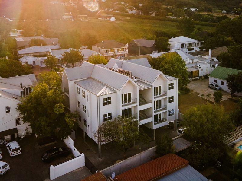 Aerial view of a multi-story apartment building featuring a metal roof, private balconies, and an integrated parking area within a residential neighborhood.