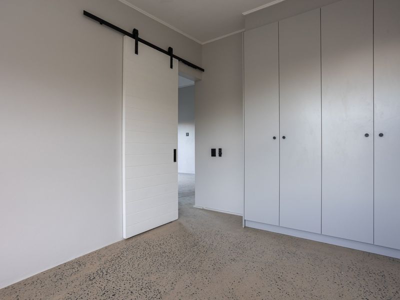 A clean, modern bedroom featuring polished concrete floors, built-in storage cupboards, and a contemporary white sliding barn door.