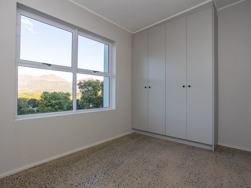 A bright, empty bedroom featuring polished concrete floors, built-in cupboards, and large windows offering scenic mountain views.