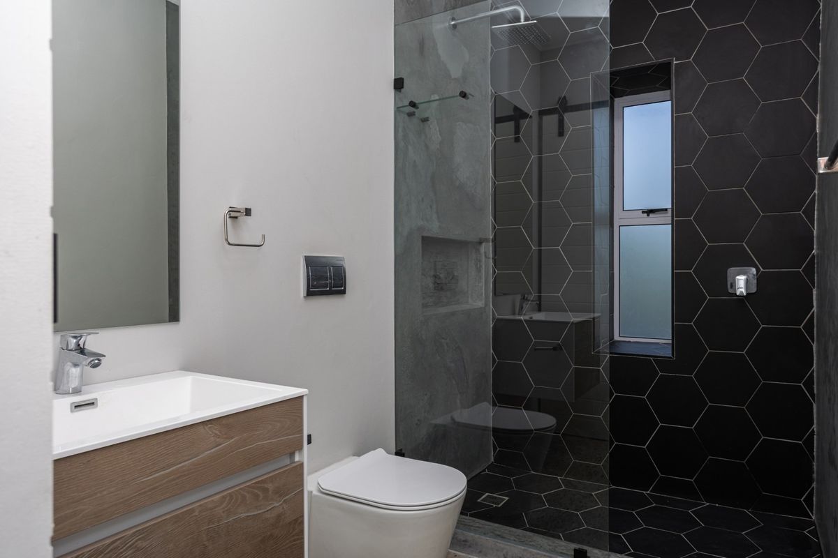 Modern bathroom featuring a wood-finish vanity, walk-in shower with black hexagonal tiling, and high-quality contemporary fixtures.