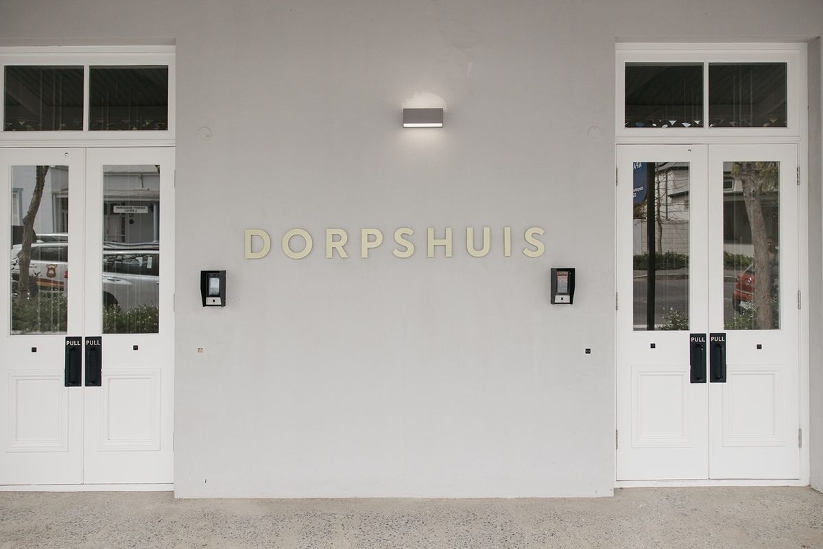 The front entrance of the Dorpshuis building featuring symmetrical double glass panel doors, modern intercom systems, and exterior wall lighting.