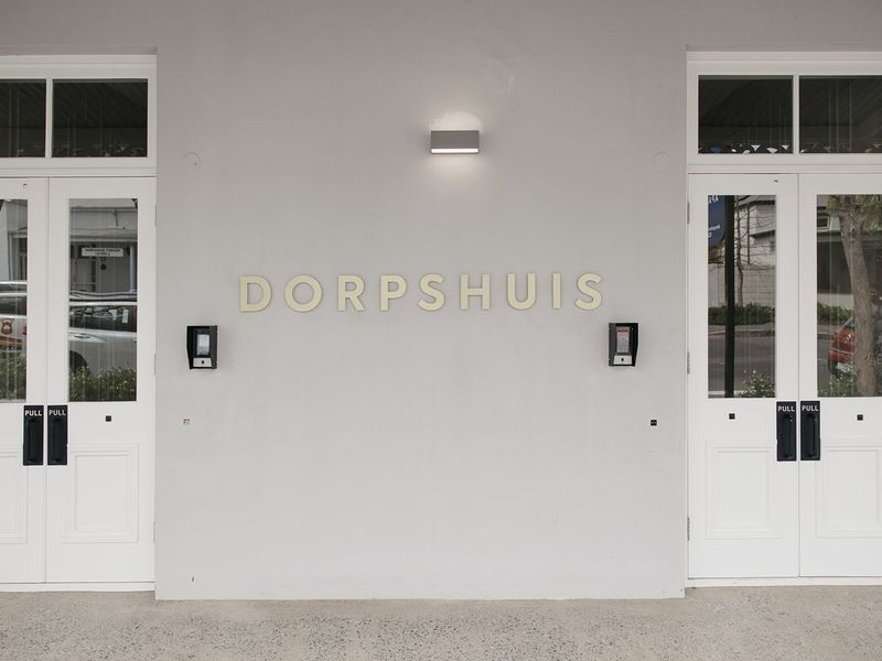 The front entrance of the Dorpshuis building featuring symmetrical double glass panel doors, modern intercom systems, and exterior wall lighting.