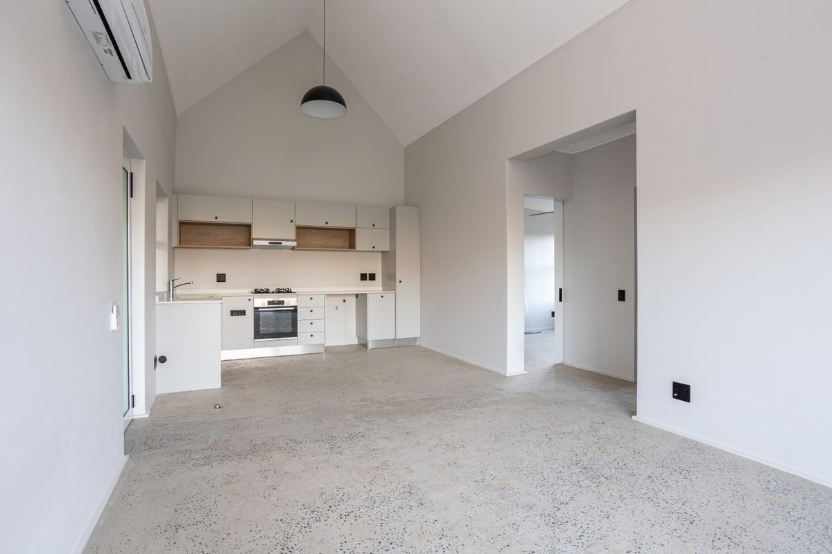 Spacious open-plan living area featuring a modern kitchen with built-in appliances, vaulted ceilings, and polished concrete flooring throughout.