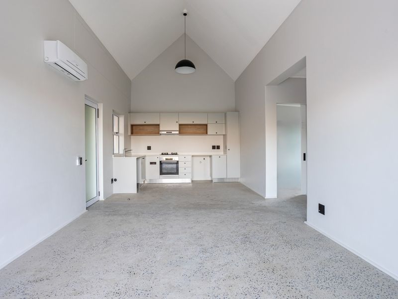 Modern open-plan living area featuring a vaulted ceiling, polished concrete floors, and a sleek, minimalist kitchen with integrated appliances.