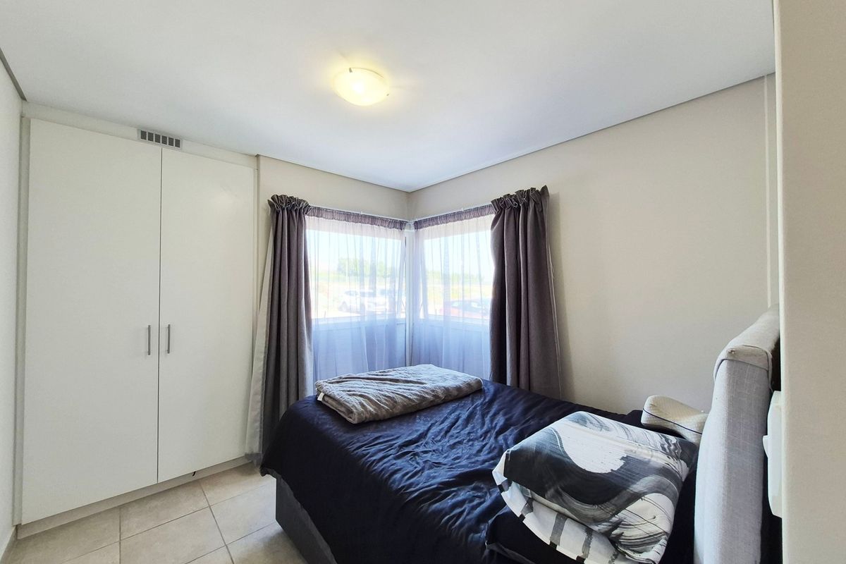 A well-lit bedroom featuring tiled flooring, corner windows for natural light, and a built-in wardrobe providing ample storage space.