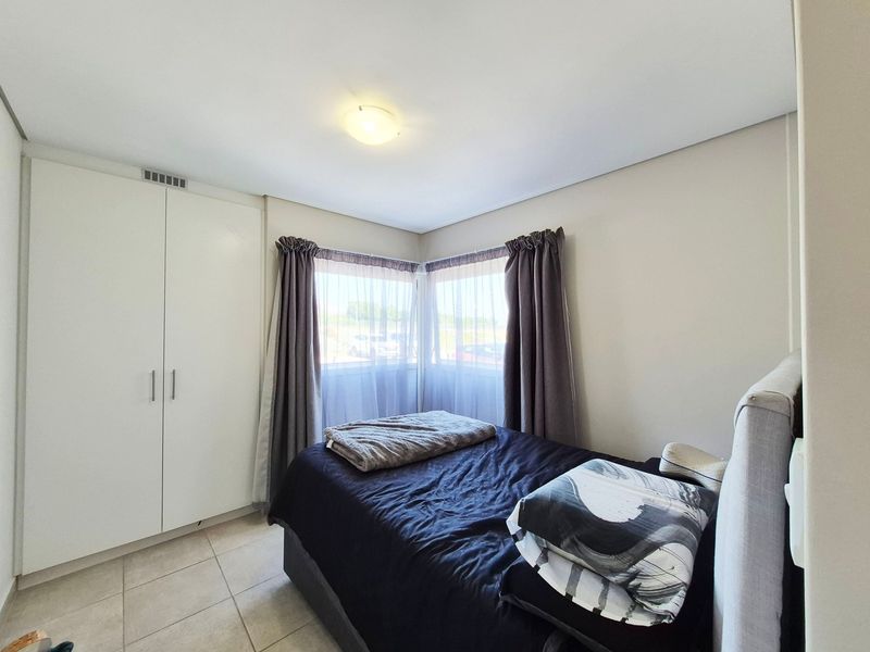 A well-lit bedroom featuring tiled flooring, corner windows for natural light, and a built-in wardrobe providing ample storage space.