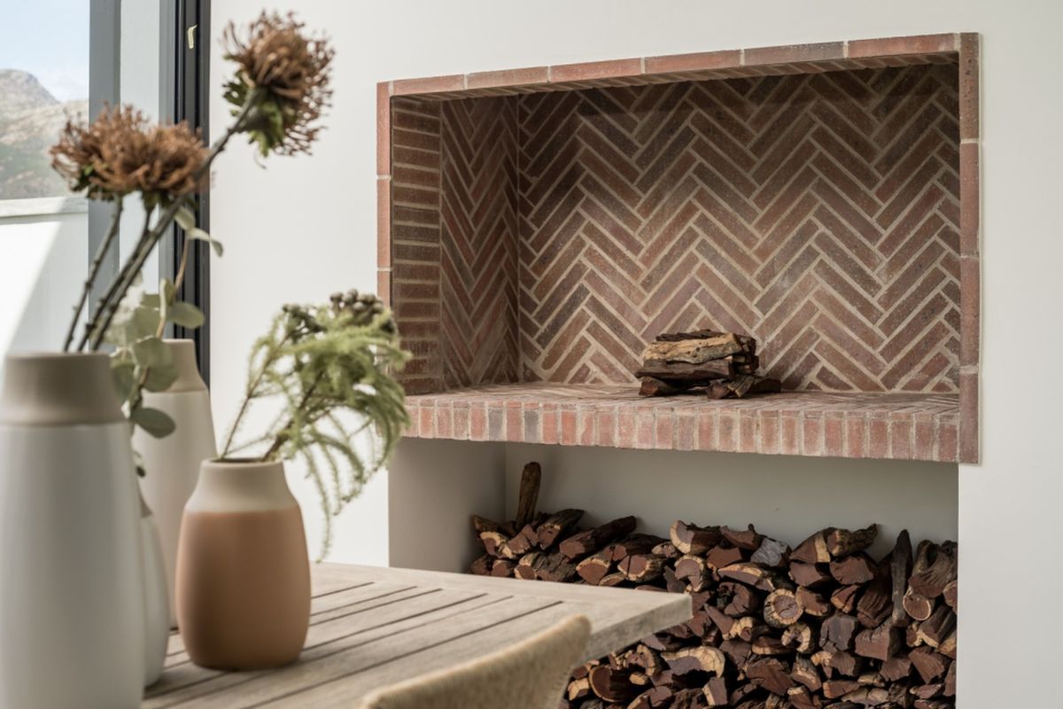 A stylish indoor fireplace featuring a decorative herringbone brick pattern and a built-in wood storage compartment.