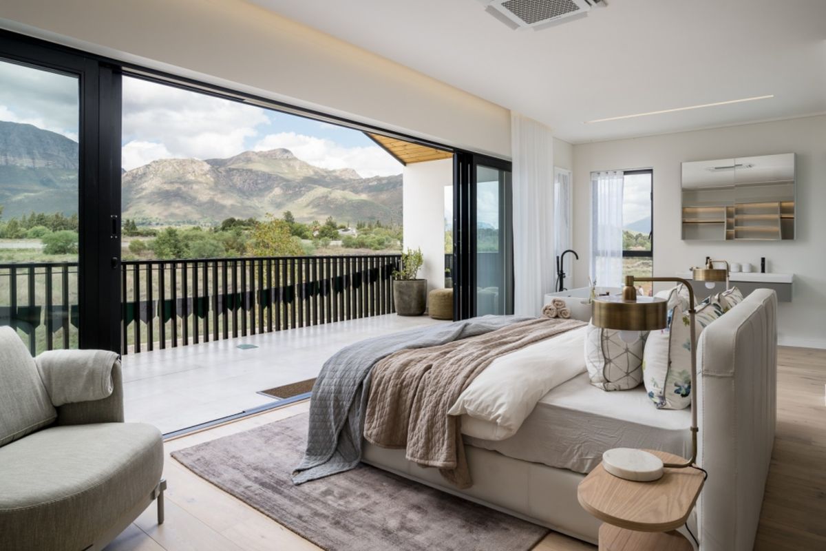 Spacious bedroom featuring large sliding glass doors opening to a private balcony with scenic mountain views and an integrated en-suite bathroom area.