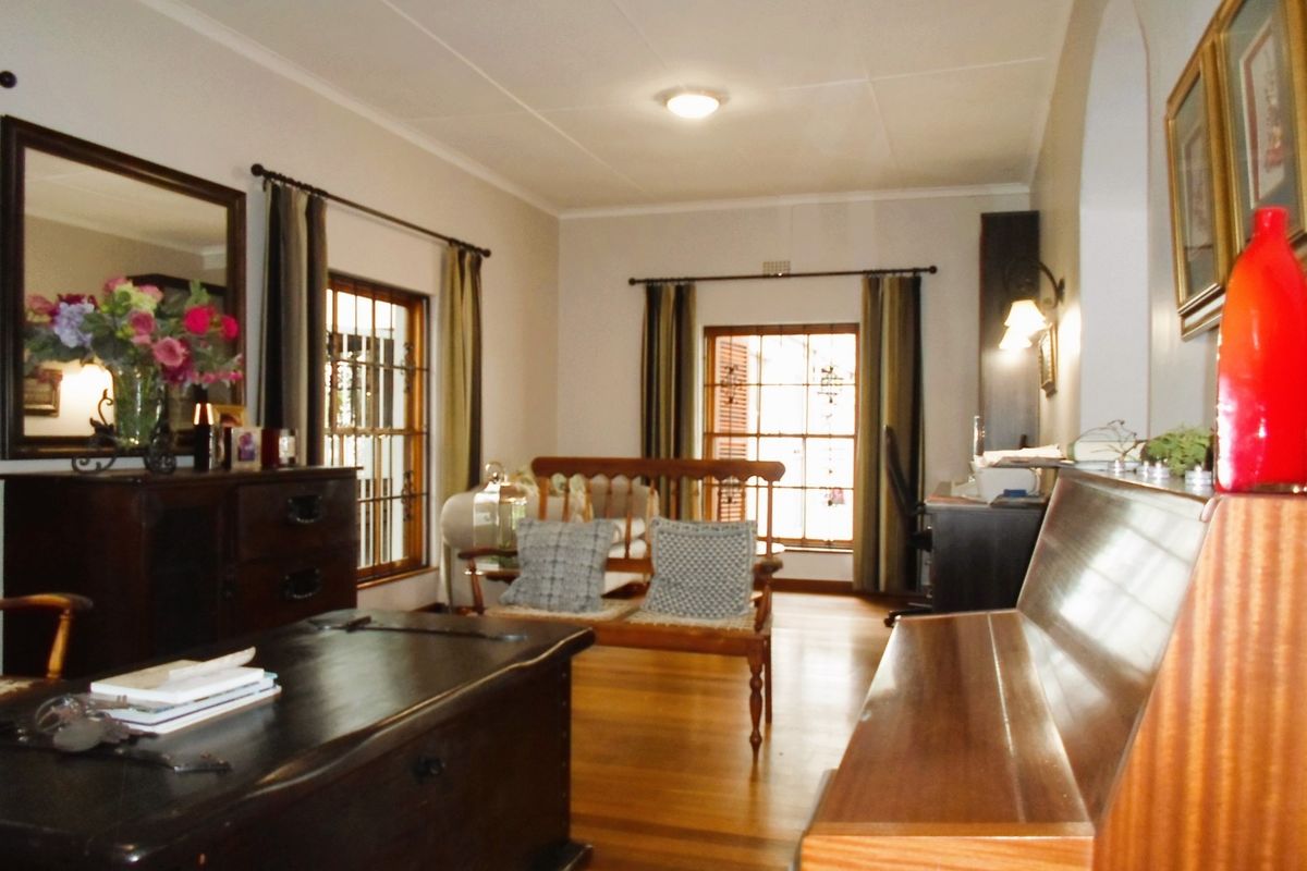A well-maintained living room featuring polished timber flooring, large windows with security bars, and classic architectural details.