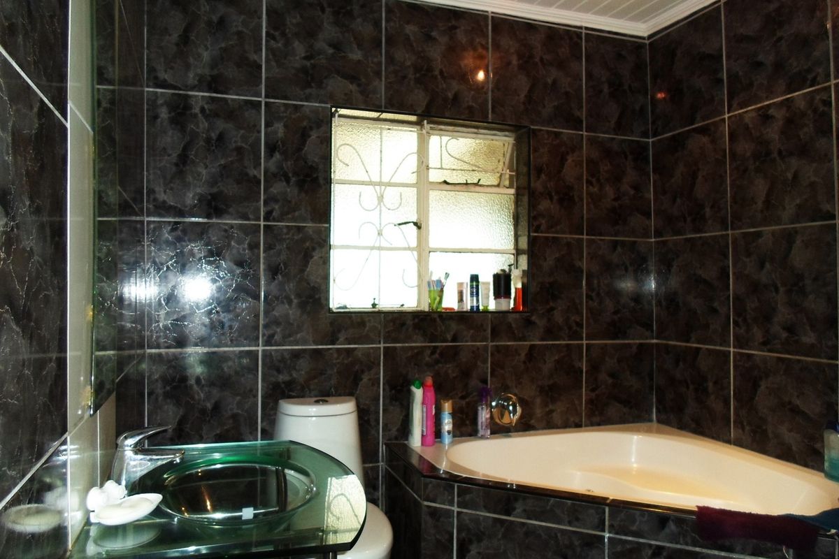 Bathroom featuring dark marble-effect wall tiles, a corner bathtub, and a modern glass vessel sink with chrome fixtures.