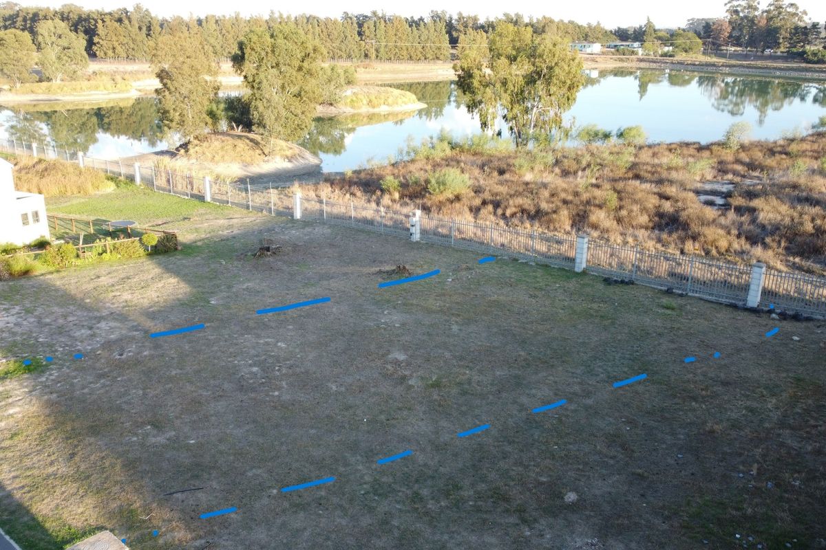 An aerial view of a vacant residential plot featuring perimeter fencing and scenic lake frontage, offering a prime location for development.