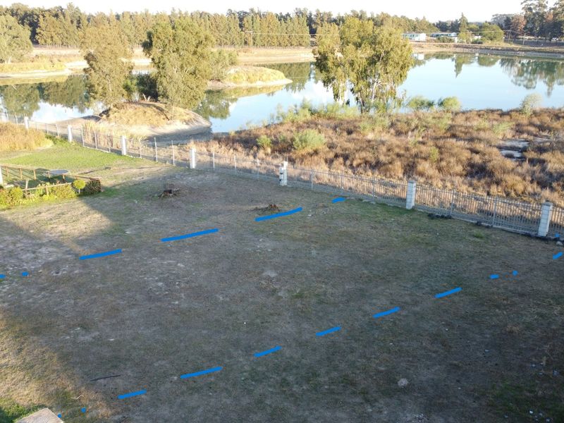 An aerial view of a vacant residential plot featuring perimeter fencing and scenic lake frontage, offering a prime location for development.