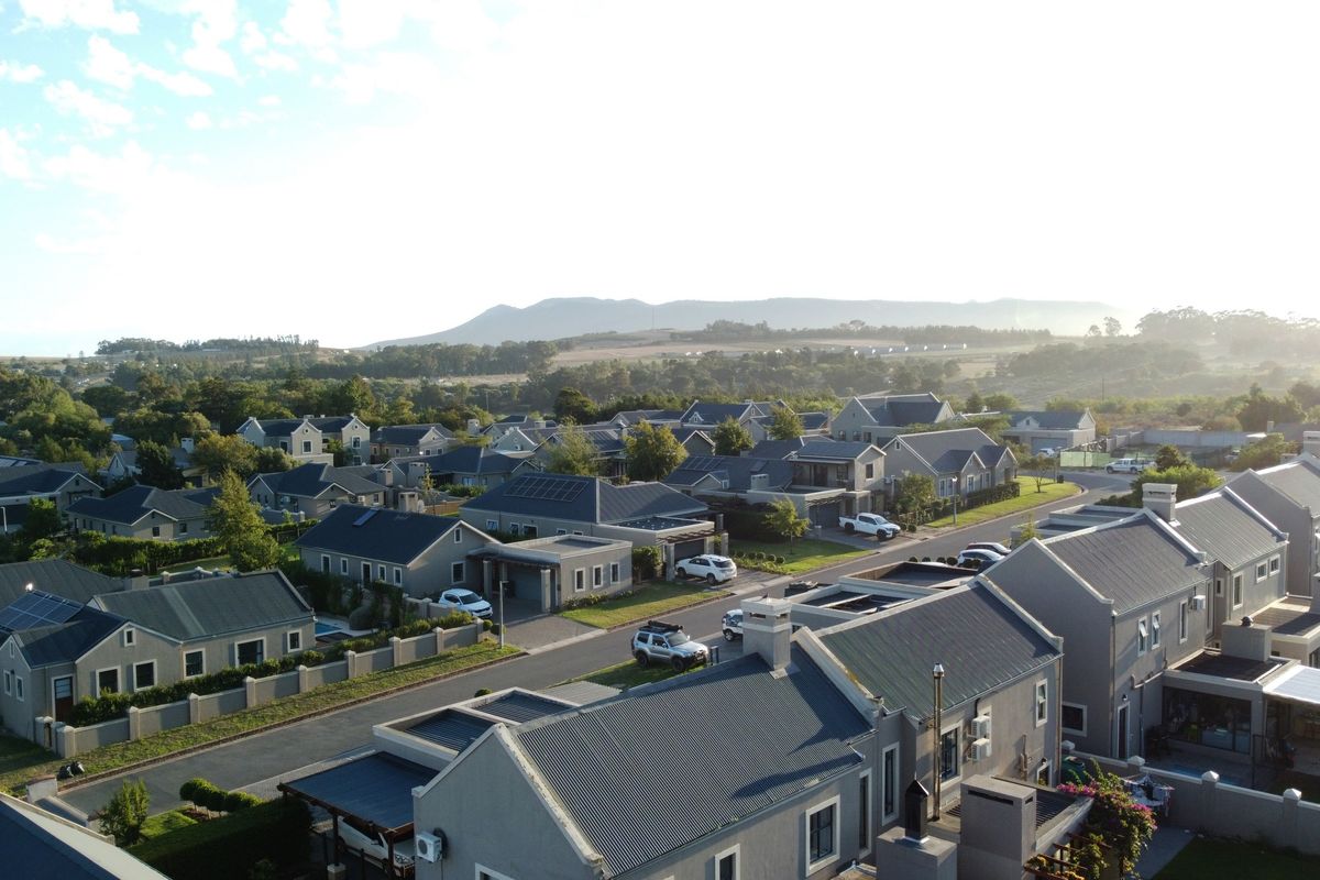 An aerial view of a residential estate featuring uniform housing architecture, paved streets, and scenic mountain views in the background.