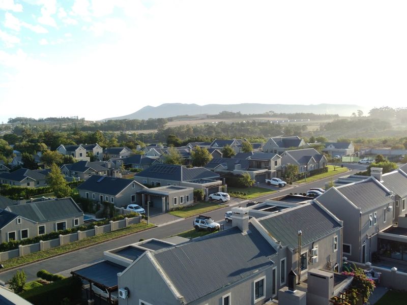 An aerial view of a residential estate featuring uniform housing architecture, paved streets, and scenic mountain views in the background.