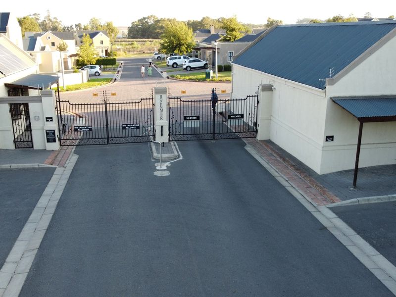Aerial view of the secure residential estate entrance featuring a gated access point, paved driveway, and well-maintained building exteriors.