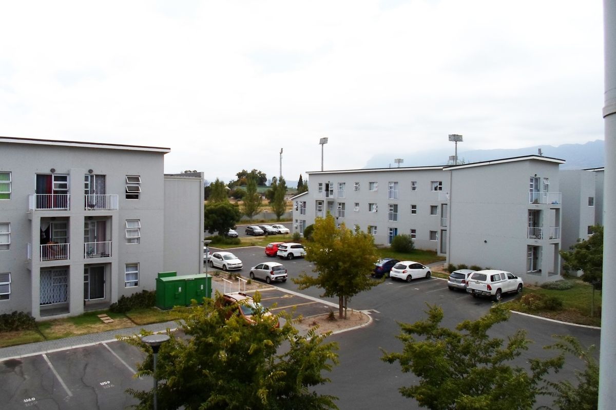 An elevated view of a residential apartment complex featuring multiple blocks, paved parking areas, and balconies.