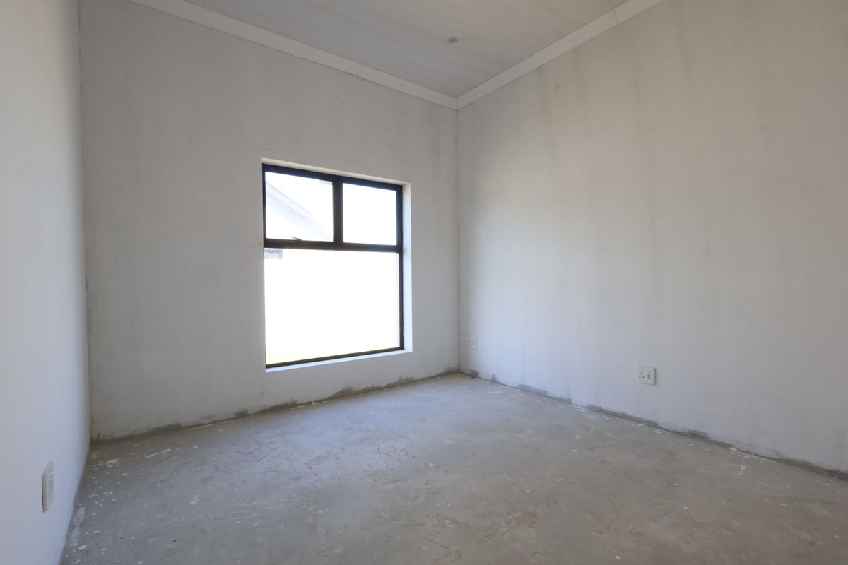 An empty, unfinished bedroom featuring plastered walls, a coved ceiling, and an aluminium-framed window, ready for final flooring and paint finishes.