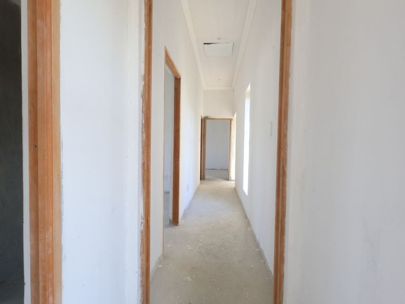 A long, unfinished hallway featuring timber door frames and ceiling access, currently in a shell state awaiting final flooring and wall finishes.