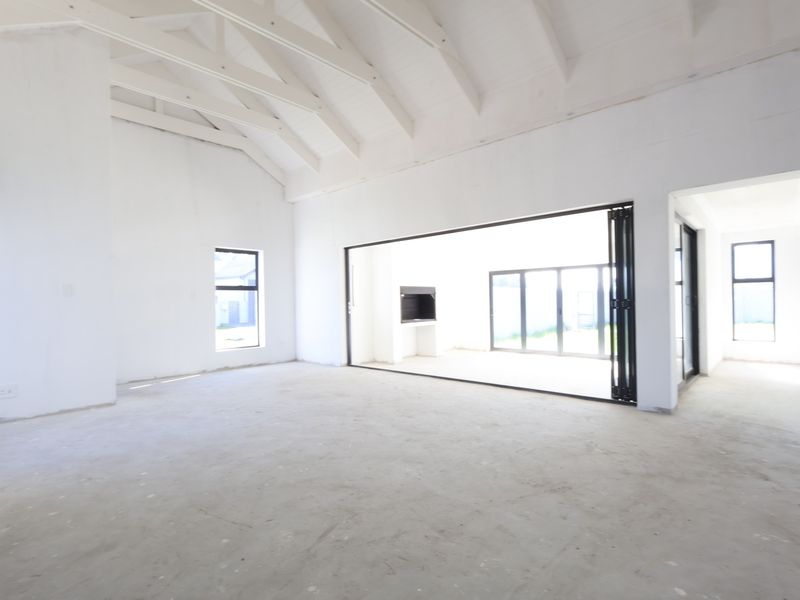 Spacious open-plan living area featuring a high vaulted ceiling with exposed rafters, built-in fireplace, and large bi-fold doors leading to the exterior.