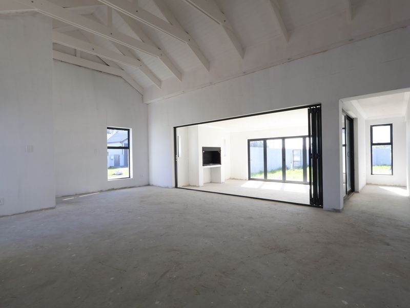 Spacious open-plan living area featuring a vaulted ceiling with exposed rafters, large bi-fold doors, and a built-in fireplace, currently in an unfinished state.