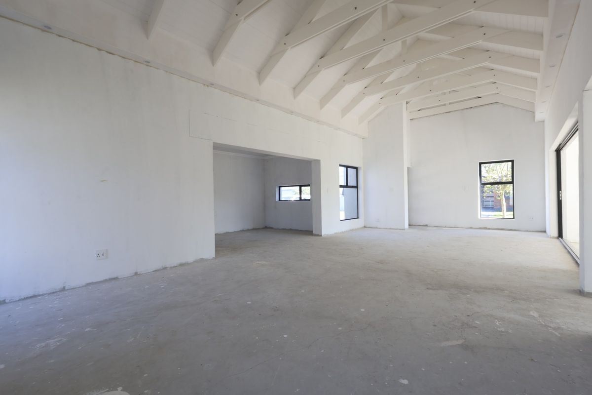 Spacious open-plan living area featuring a high vaulted ceiling with exposed rafters, large windows, and sliding doors, currently in an unfinished state.