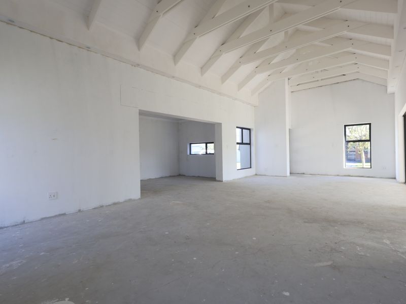 Spacious open-plan living area featuring a high vaulted ceiling with exposed rafters, large windows, and sliding doors, currently in an unfinished state.