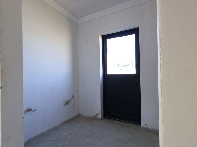 An unfinished utility or laundry space featuring exposed plumbing connections, a black external door, and bare wall surfaces ready for final finishes.