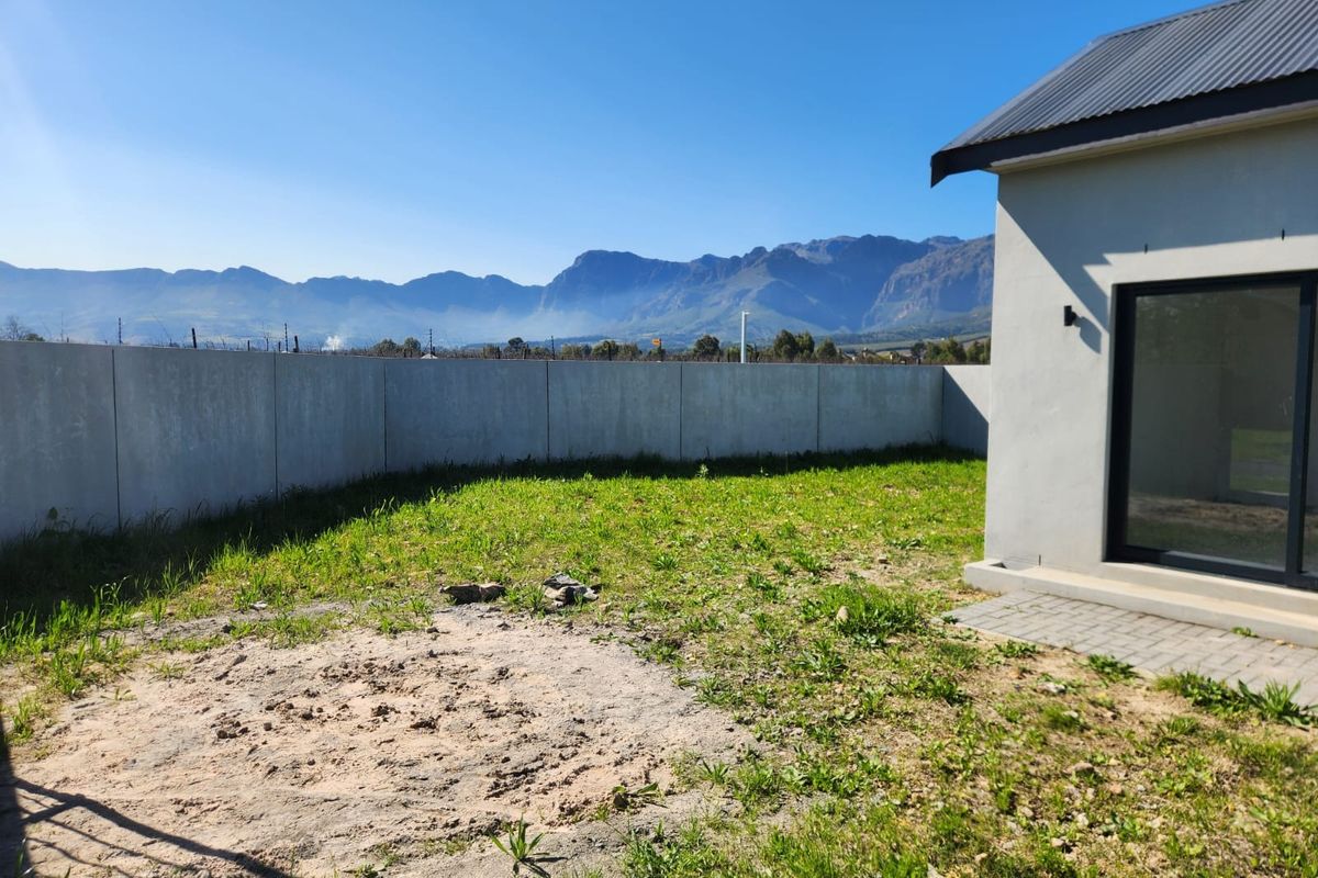 Rear exterior view featuring a paved patio, a large unlandscaped garden area, and a concrete boundary wall with scenic mountain views.