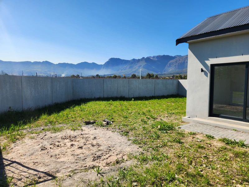 Rear exterior view featuring a paved patio, a large unlandscaped garden area, and a concrete boundary wall with scenic mountain views.