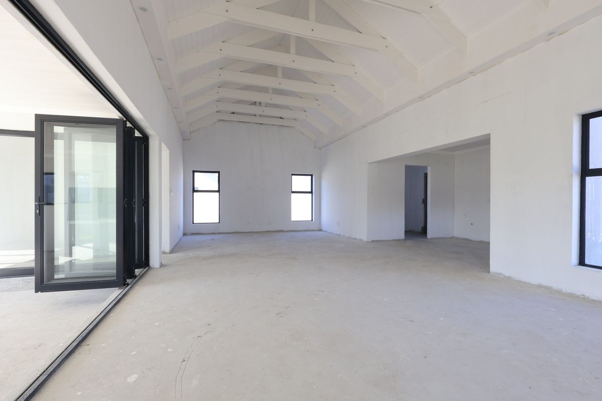 Spacious open-plan living area featuring a high vaulted ceiling with exposed trusses, large aluminium stacker doors, and unfinished interior finishes ready for completion.
