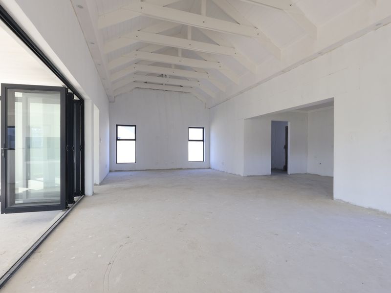 Spacious open-plan living area featuring a high vaulted ceiling with exposed trusses, large aluminium stacker doors, and unfinished interior finishes ready for completion.