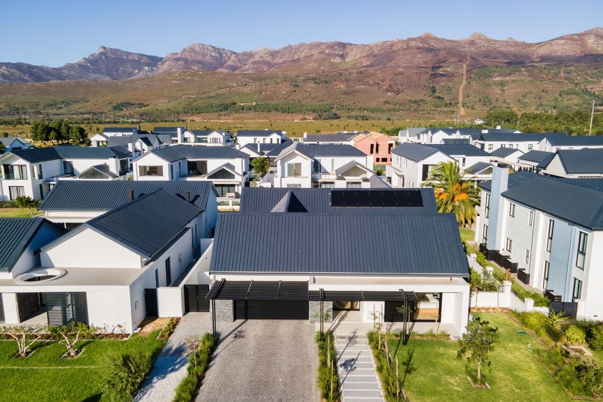 Aerial view of a modern residential property featuring a metal roof with solar panels, a paved driveway, double garage, and a well-maintained garden.
