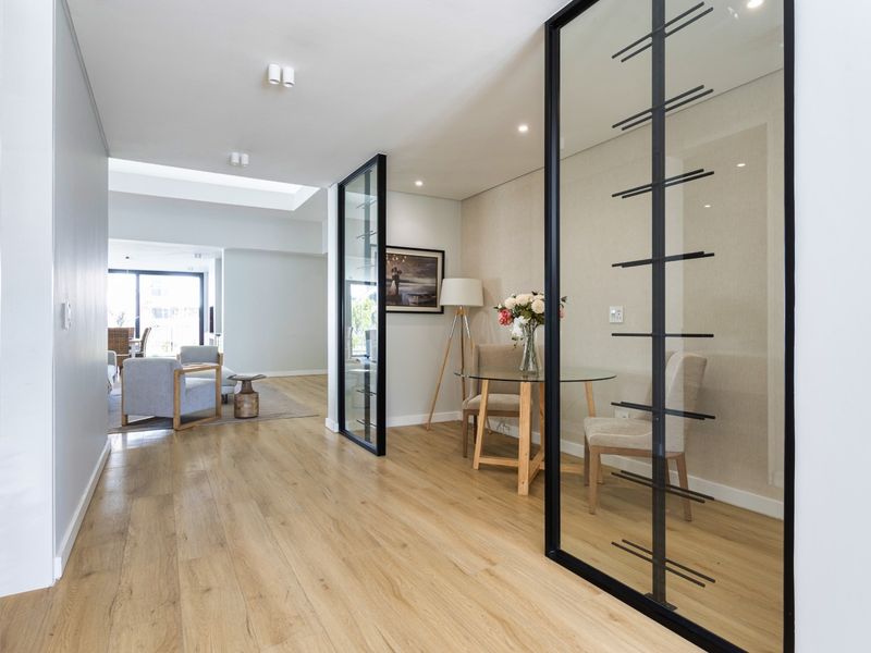 A modern, bright hallway featuring timber flooring, a stylish glass partition wall, and a skylight, leading into an open-plan living area.