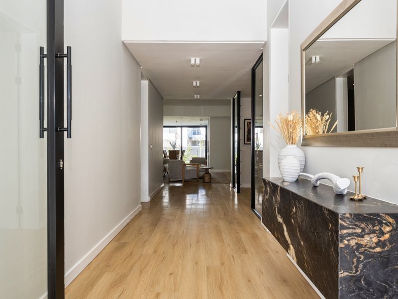A bright and modern hallway featuring timber flooring, recessed downlighting, and a sleek black-framed glass door leading to the living area.