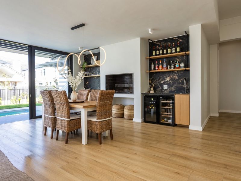 Modern open-plan living area featuring a built-in fireplace, custom bar with stone backsplash, integrated wine coolers, and seamless access to the outdoor pool area.